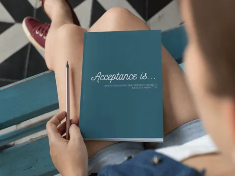 Person holding a blue booklet titled "Acceptance is..." while seated on a geometric patterned surface