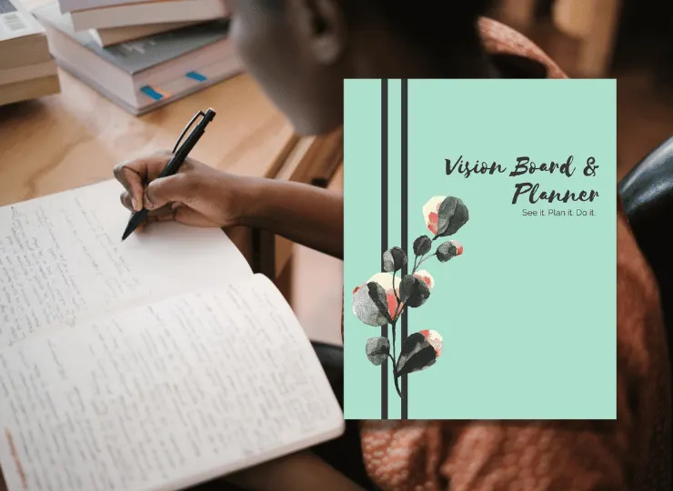Person writing in a notebook at a wooden desk with books and a vision board planner nearby
