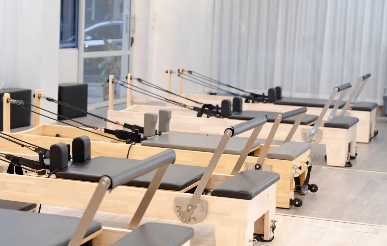 A row of wooden Pilates reformers in a bright, empty studio.