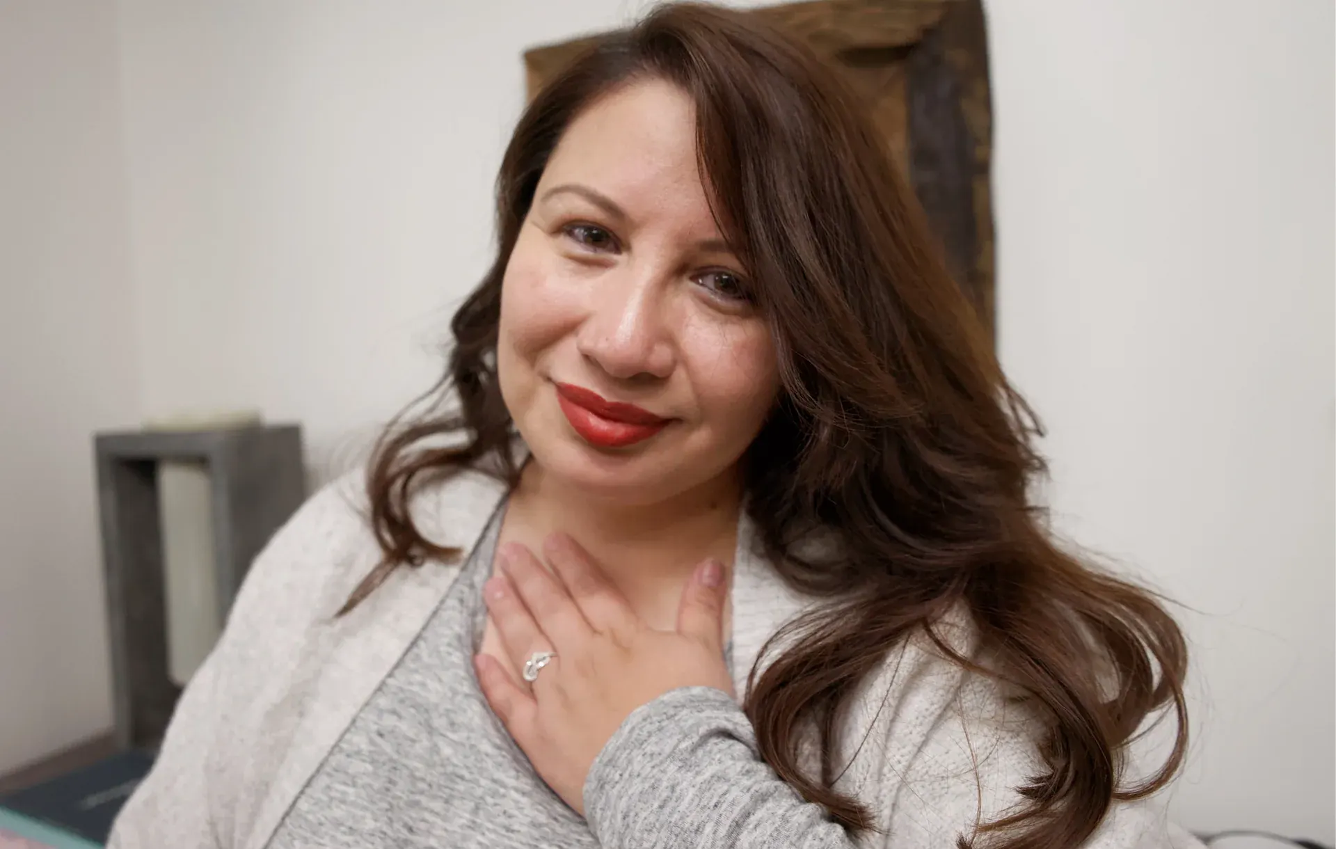 Sofia Mendoza rests a hand on her chest with a gentle smile indoors