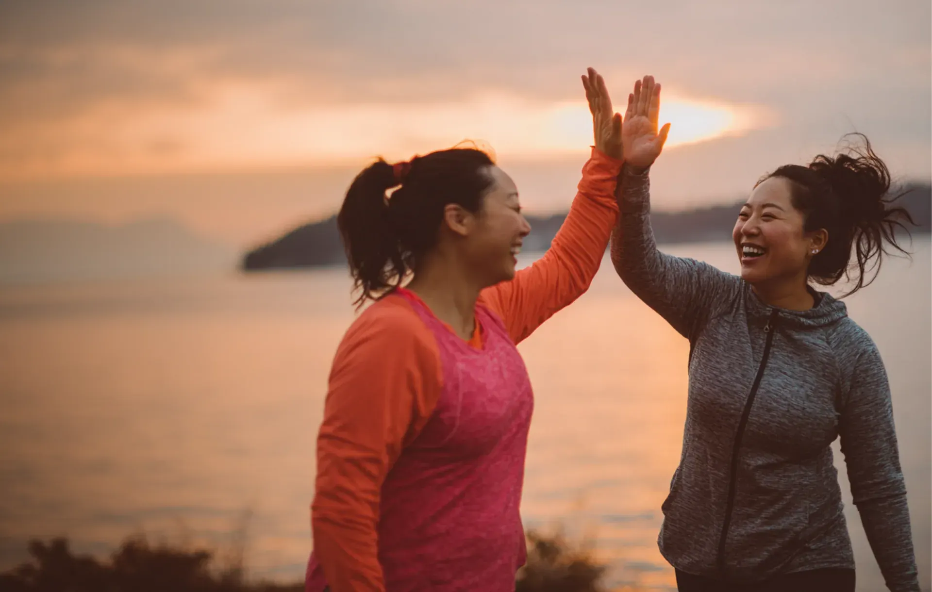 Two women share a high five on the beach at sunset