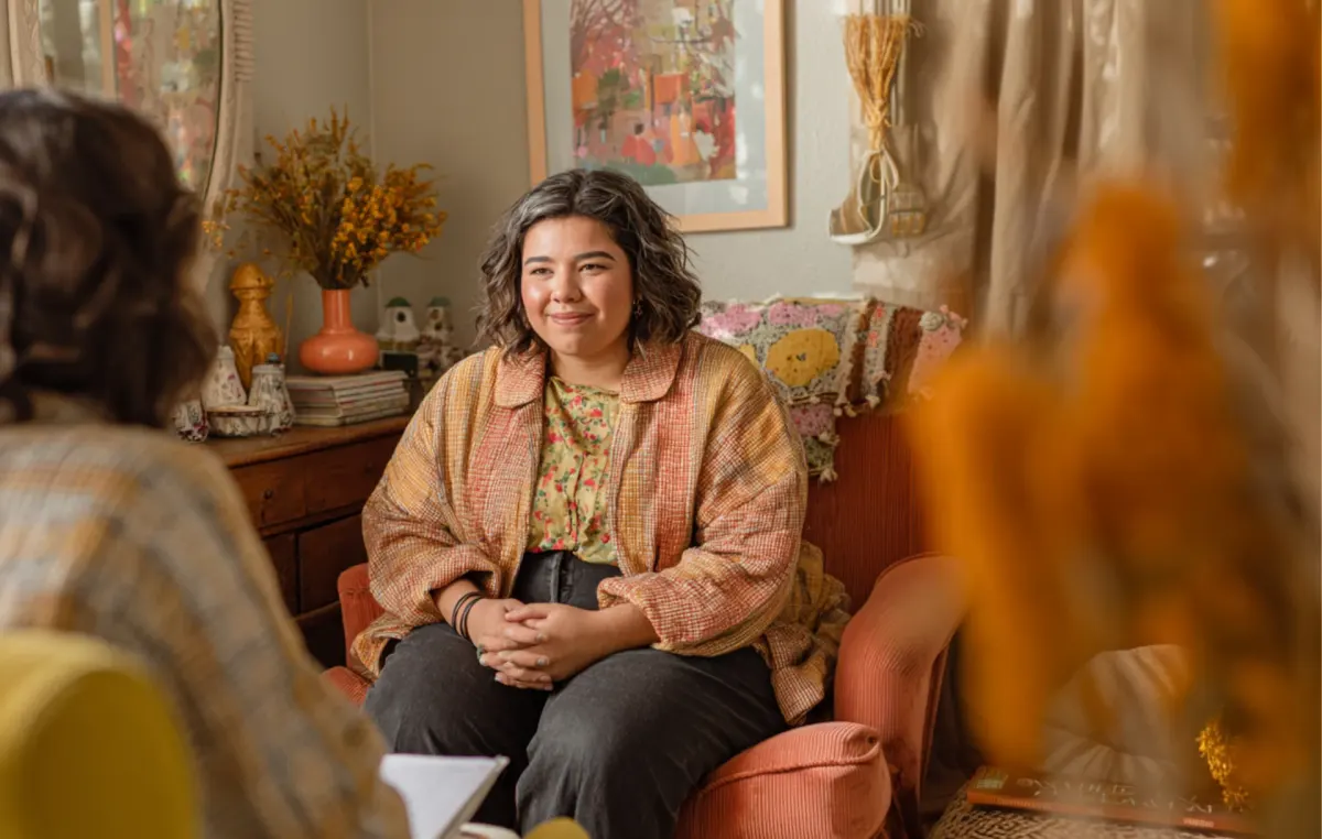 Two women sit in conversation, one in a supportive listening posture, in a warm room