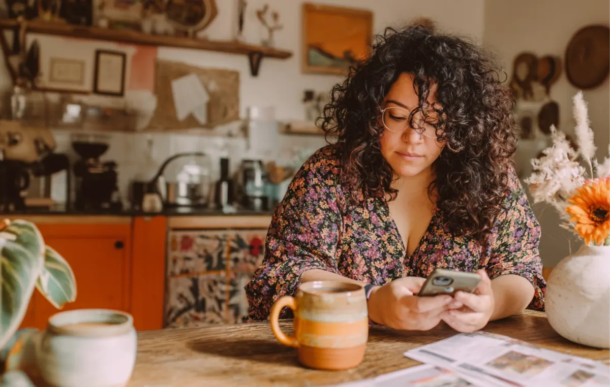 A woman with curly hair sits reading at a table in a colorful eclectic kitchen
