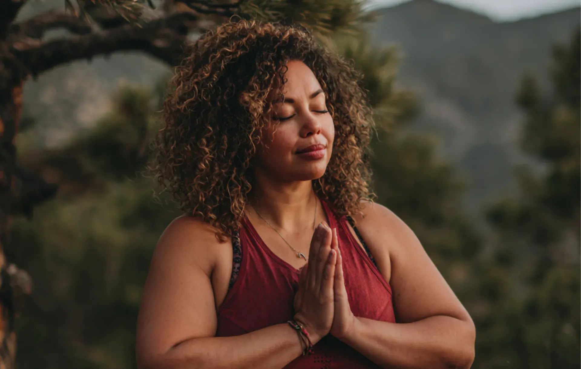 A woman meditates with hands pressed together in a forest setting